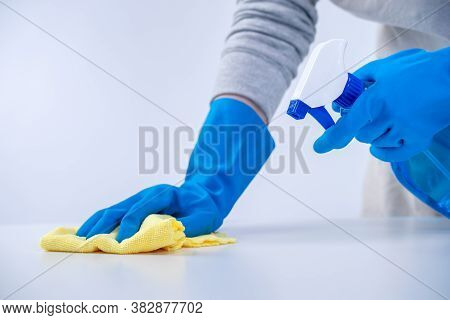 Young Woman Housekeeper In Apron Is Cleaning, Wiping Down Table Surface With Blue Gloves, Wet Yellow