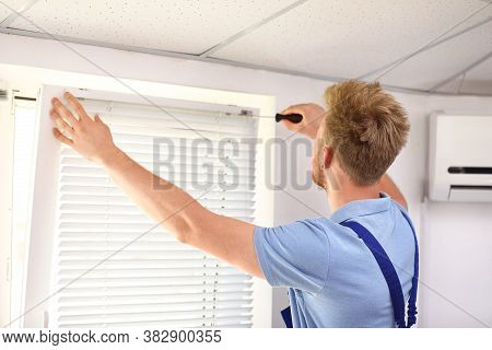 Handyman With Screwdriver Installing Window Blinds Indoors