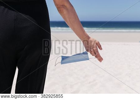 Female Hand Holding A Wind-swept Medical Mask With The Sea In The Background