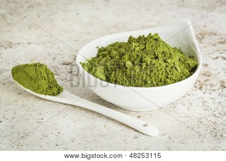 Moringa list prášek v malé misce se lžící proti keramické dlaždice pozadí