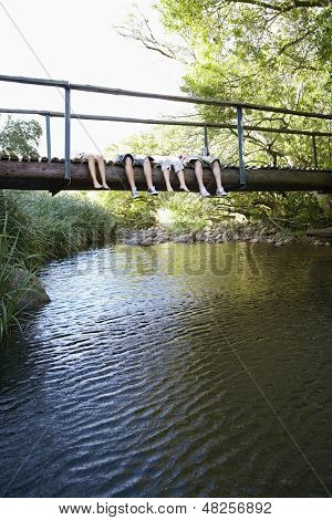 Sección baja de adolescentes y niñas mintiendo sobre el puente de madera sobre el río