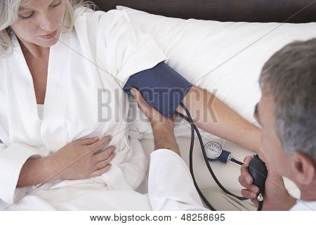 Ginecologo prendendo la pressione arteriosa del paziente femminile a casa di età medio