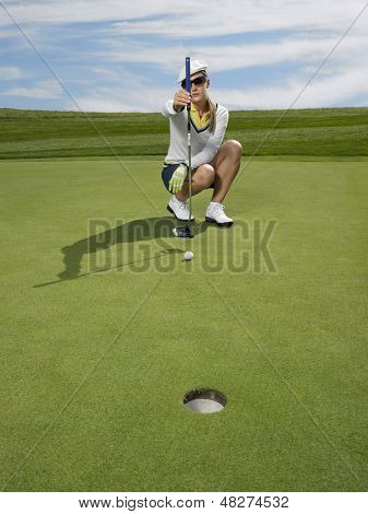 Full length of female golfer lining up a putt in golf course