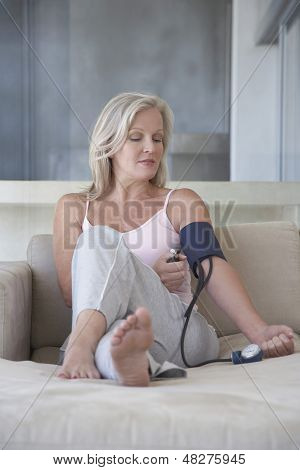 Medio di età donna controllo pressione sanguigna con sphygmometer sul divano
