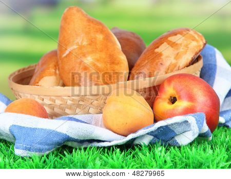 Empanadillas al horno frescas con frutos, en canasta de mimbre, sobre hierba, sobre fondo brillante