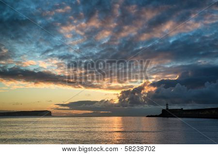 Beautiful Vibrant Sunrise Sky Over Calm Water Ocean With Lighthouse And Harbor Wall