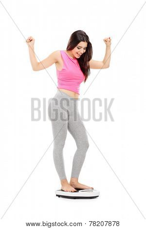 Full length portrait of a joyful girl standing on a weight scale isolated on white background