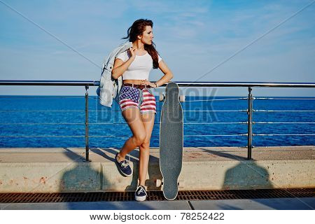 Young fashion woman standing with wooden longboard at sunset
