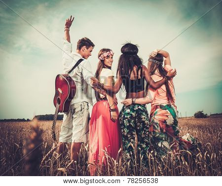Multi-ethnic hippie friends with guitar in a wheat field 