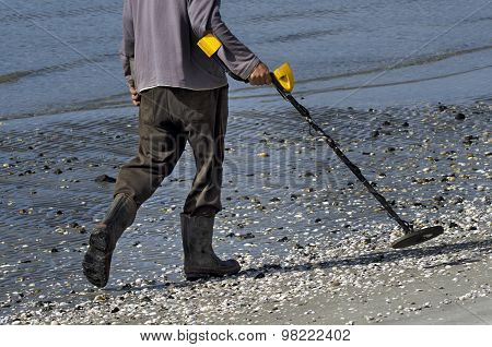 Unrecognizable Man using a metal detector on the beach.