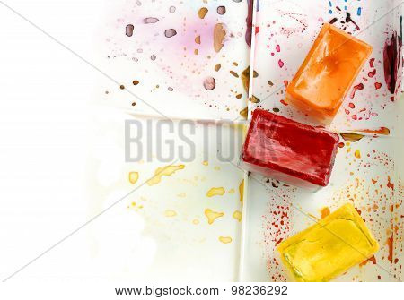 Tree bright watercolor cases on a paint box with colorful splashes