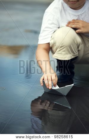 boy play in paper ship in water puddel