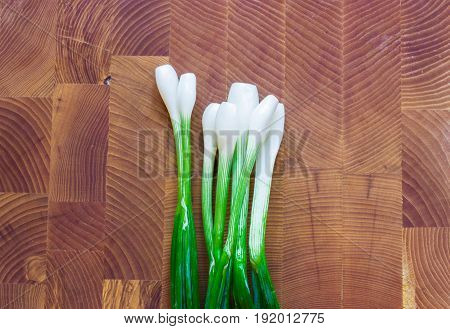 A bunch of fresh green onions on a wooden board.