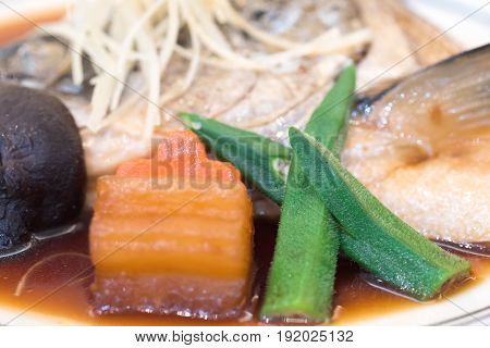 Vegetable on boiled salmon head in sweet soy sauce served with carrot mushrooms okra radishes and ginger in a Japanese restaurant.