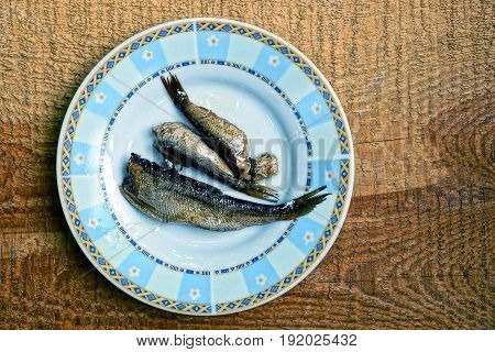 Three small fish on a white plate on a brown wooden board