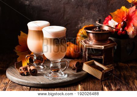 Two glasses pumpkin spicy latte with whipped cream and cinnamon on a wooden stand