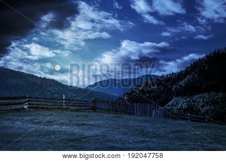 Fence Through The Grassy Meadow In Mountains At Night In Full Moon Light