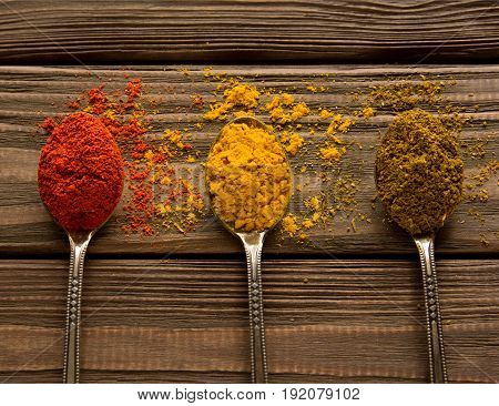 Spice powder on a wooden background. Three spoons with various spices. Close-up. Top view.