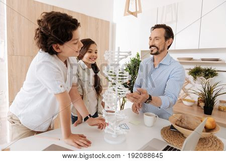 Science is exciting. Adorable close-knit family standing around a big white 3D DNA model examining it from different sides with his father touching one of the nucleotides