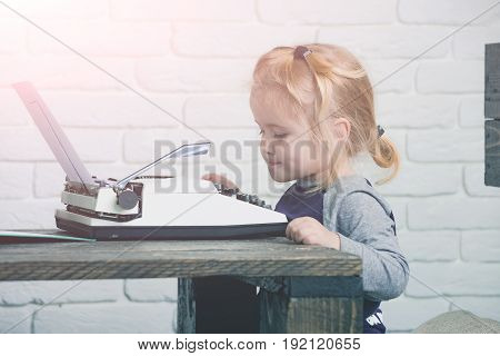 Kid Sitting At Table And Typing Typewriter With Paper