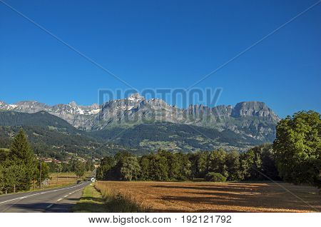 Fields, road, forest, alpine landscape and blue sky in the background, Saint-Gervais-Les-Bains, French Alps