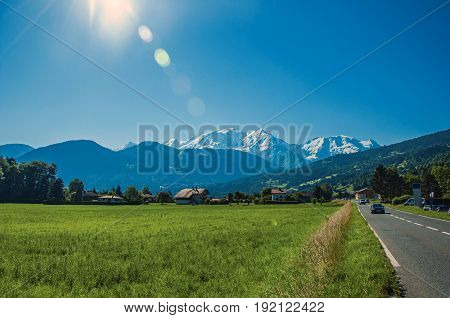Fields with houses and road, forest, alpine landscape and blue sky in the background, Saint-Gervais-Les-Bains, French Alps
