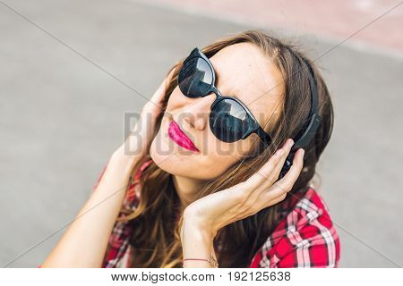 Young smiling woman relaxing and listening to music with headphones in the street