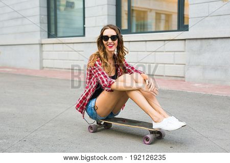 Young woman sitting on the skater. Smiling woman with skateboard in outdoors.