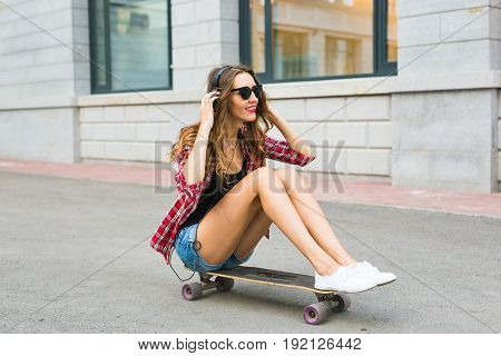 Young woman sitting on the skater. Smiling woman with skateboard in outdoors.