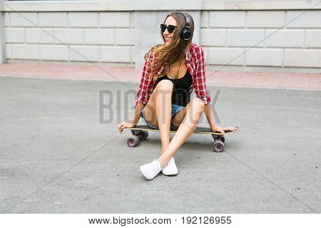 Young woman sitting on the skater. Smiling woman with skateboard in outdoors.