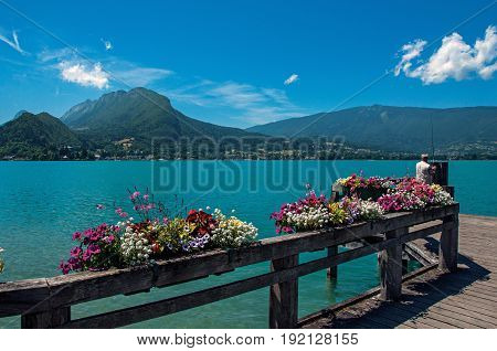 Pier with flowers on the lake of Annecy, in the village of Talloires. Mountains landscape and blue sky on background. France