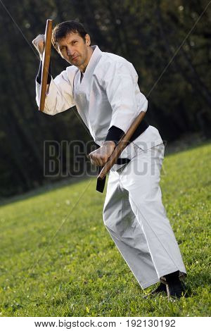 The ninja in white kimono is practicing with tonfa outdoors.