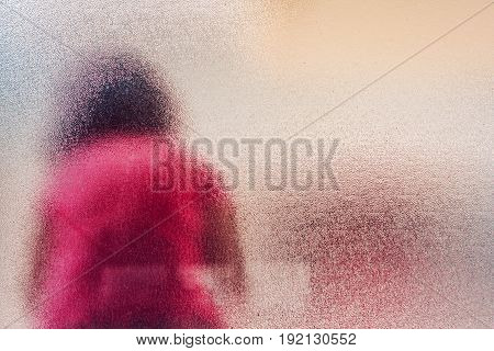 Silhouette of unrecognizable sad autistic girl behind stained glass window sitting alone in the backyard