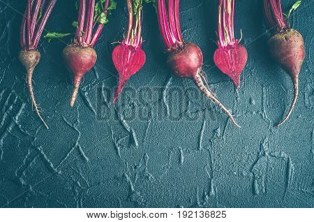 Row of homegrown organic young beets with green leaves on dark stone table. Food background. Concept of healthy eating. Toned image. Top view. Copy space.