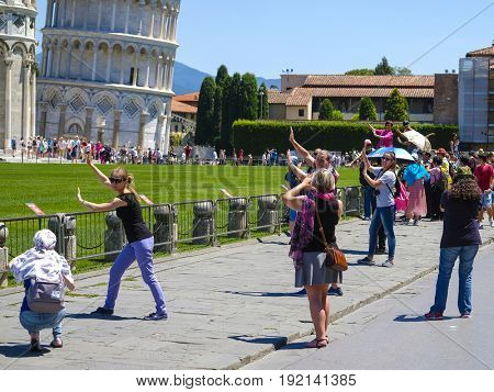 Pisa, Italy - June, 15, 2017: tourists try to be photographed against the background of the well-known falling tower in Pisa, Italy so that it seemed that they support tower