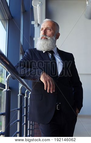 Vertical of pokerfaced man age of 50-60 looking out window while leaning on handrail