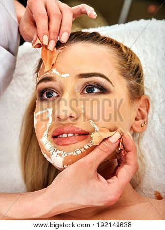 Collagen face mask. Facial skin treatment. Woman receiving cosmetic procedure in beauty salon. Bottle with moisturizing cream on background. Cropped shot of removing wrinkles. Mask against black dots.
