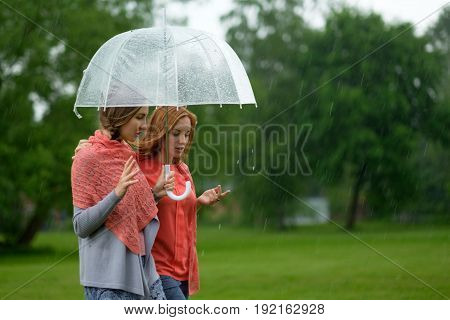 Two women walking park in rain and talk. Friendship and people communication. Rainy day in summer