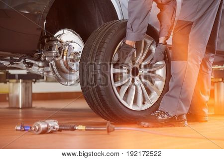 Low section of male mechanic repairing car's tire in repair shop
