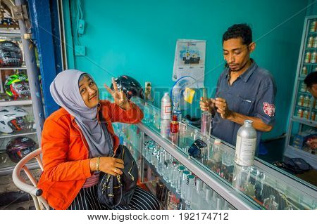 BALI, INDONESIA - MARCH 08, 2017: Unidentified man using syringes and pipettes mixing essences to prepare perfumes, while a woman is buying a perfume in the perfume store in Denpasar Indonesia.
