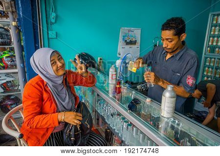 BALI, INDONESIA - MARCH 08, 2017: Unidentified man using syringes and pipettes mixing essences to prepare perfumes, while a woman is buying a perfume in the perfume store in Denpasar Indonesia.