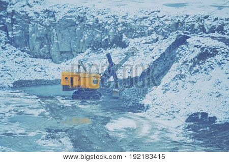 big huge yellow excavator in a granite quarry in winter. huge loading shovel bucket stands on a granite floor strewn with snow in his career on a winter day