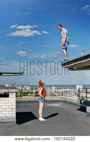 A loving couple of roofer on the roof. The guy and the girl are looking at each other. Romance and courage. An unusual date.
