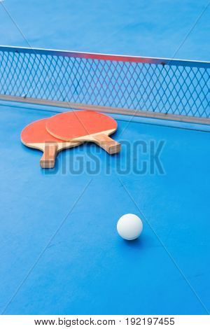 pingpong rackets and ball and net on a blue pingpong table