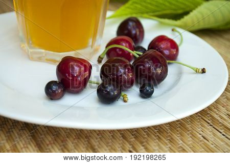 ripe cherry on a white plate with glass of juice