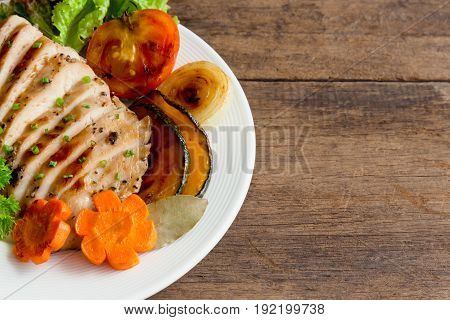 Sliced chicken breast barbecue on white plate served with grilled vegetable. Delicious chicken breast steak and salad for dinner. Homemade chicken breast barbecue on wood table for background. Chicken barbecue or pork steak.