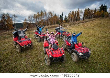 Young People In Winter Clothes With Raised Hands Up On Red Atv Off-road Vehicles On A Countryside Tr