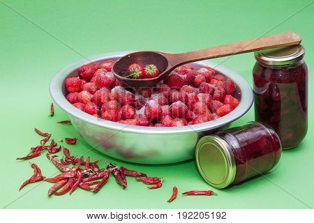 Strawberries from the manufacturer with sugar and jars for making jam on a green background.