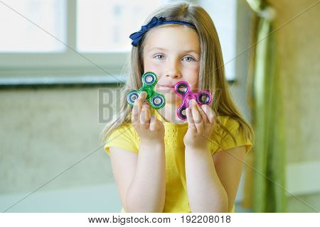 Little Beautiful Girl In Yellow T-shirt Is Playing With Two Spinners In Hands