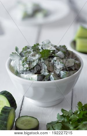 Cucumber salad with coriander and yogurt dressing on the white wooden background. Close up